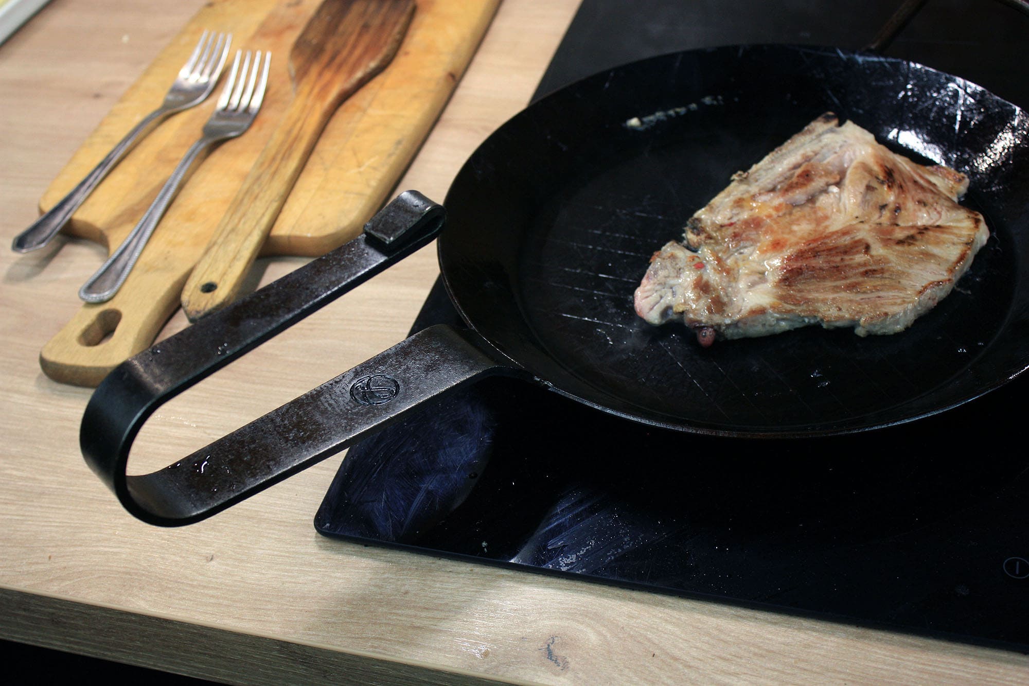Die beste Eisenpfanne 189 Eine Hand hebt die Leutner PAN Ø 28 cm am gebogenen Griff an, während ein Schweinesteak in der Pfanne liegt.