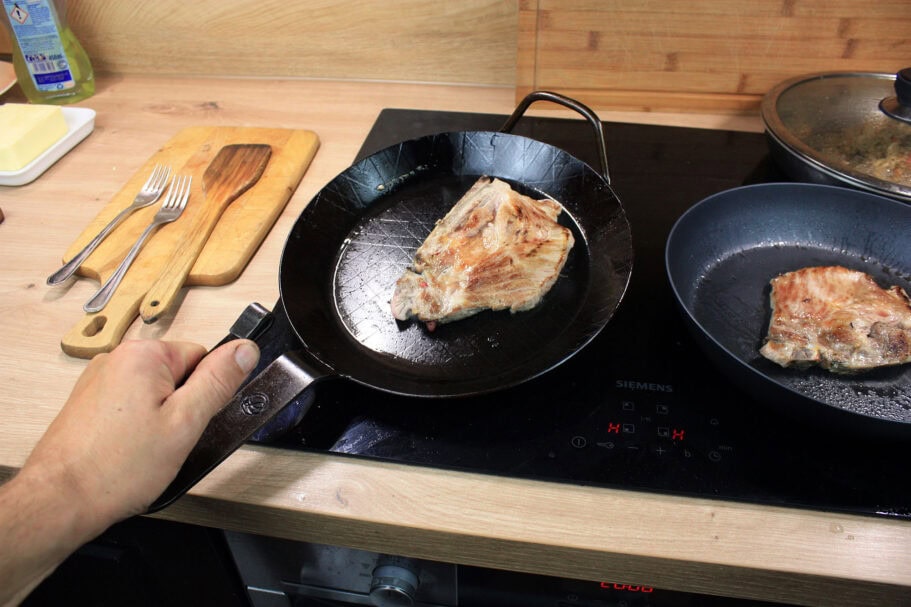 Die beste Eisenpfanne 194 Eine Hand hebt die Leutner PAN Ø 28 cm mit einem gebratenen Schweinesteak vom Induktionskochfeld.