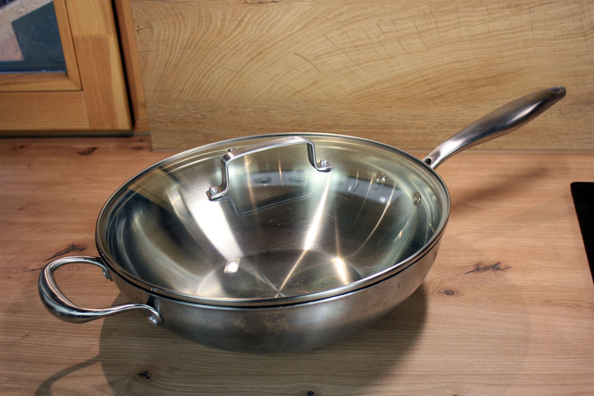 Die beste Wokpfanne 171 Leerer Edelstahl-Wok mit flach ansteigender Wandung, langem Griff und seitlichem Hilfsgriff.