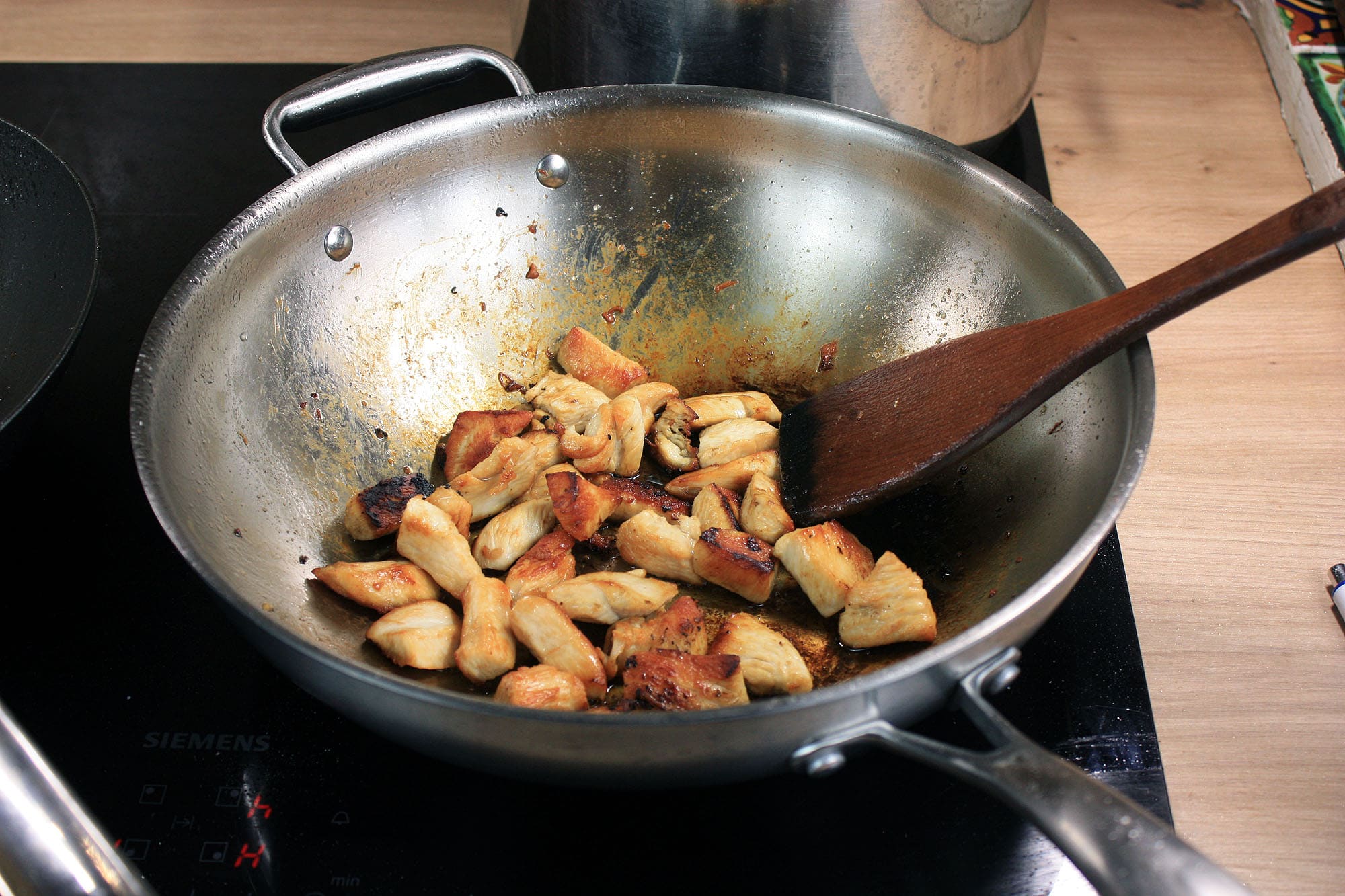 Die beste Wokpfanne 172 Gebräunte Stücke Hähnchenfleisch braten auf dem Boden des Edelstahl-Woks.