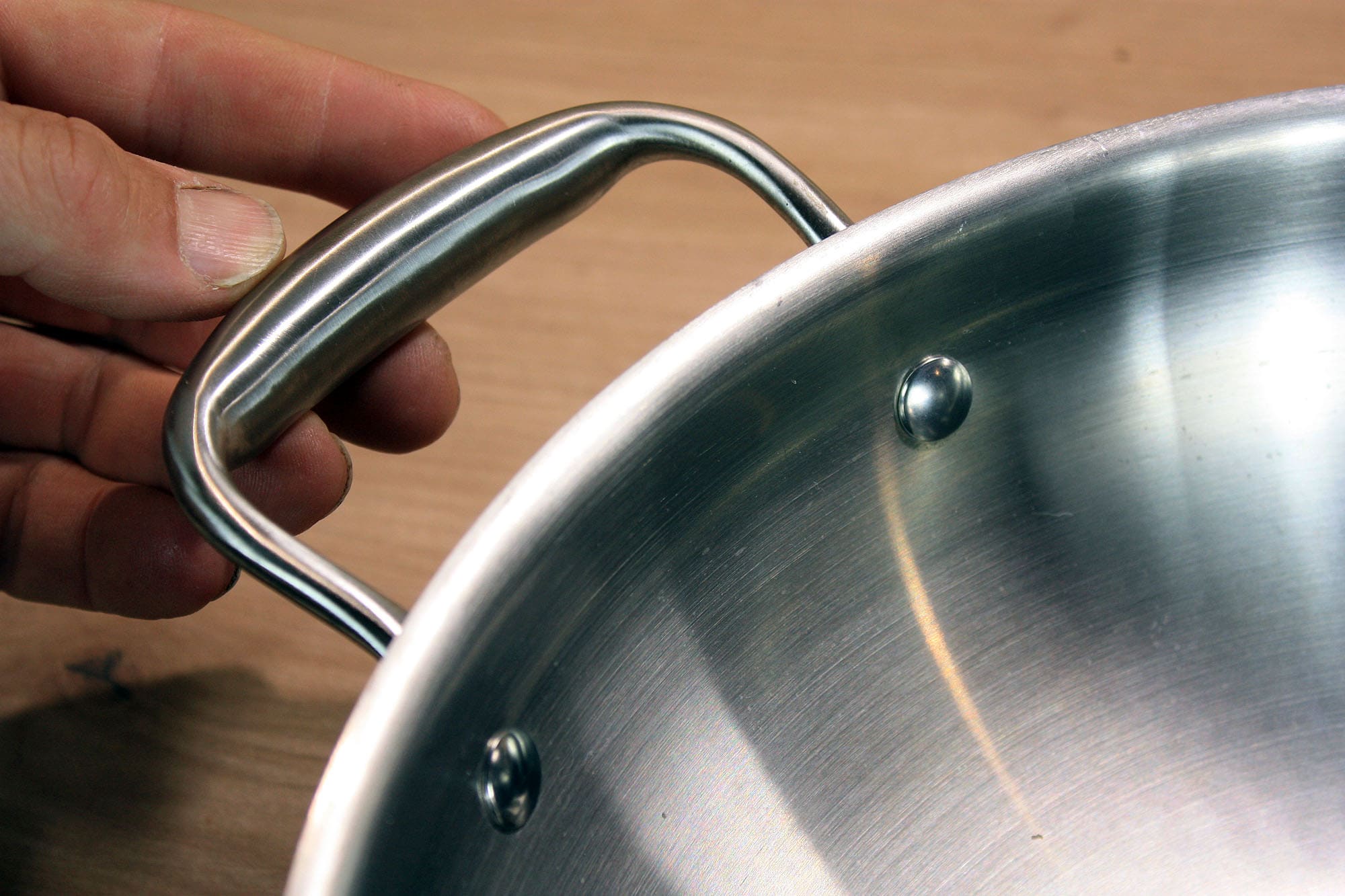 Die beste Wokpfanne 176 Nahaufnahme des seitlichen Hilfsgriffs aus Edelstahl am Wok, der von einer Hand gehalten wird.