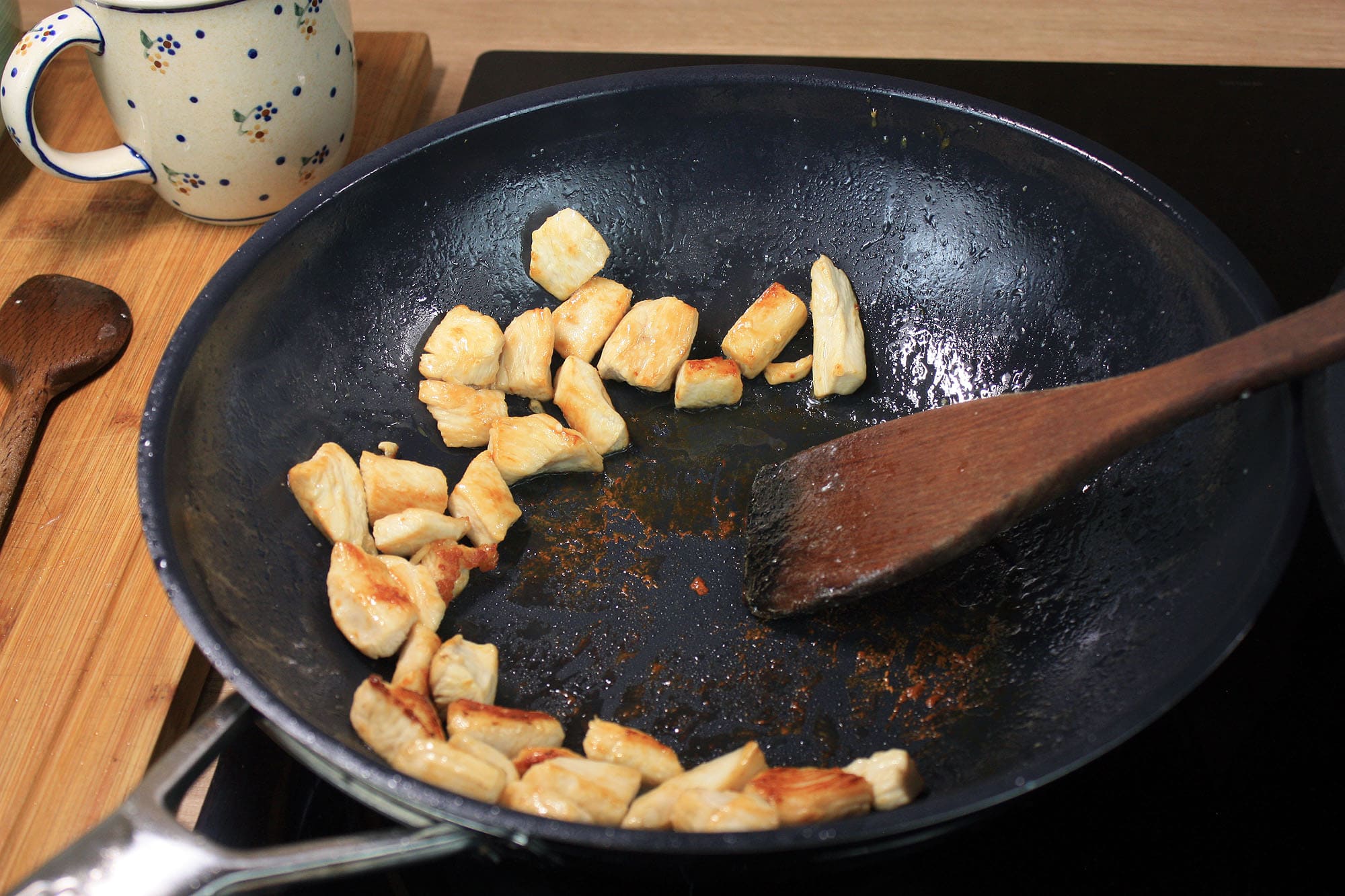 Die beste Wokpfanne 204 Goldbraun gebratene Hähnchenstücke liegen auf der Bratfläche der Wokpfanne.