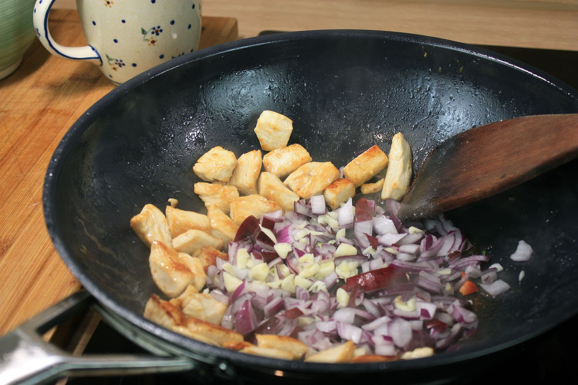 Die beste Wokpfanne 205 Gebräuntes Hähnchen und gewürfelte Zwiebeln werden in der Wokpfanne gebraten.